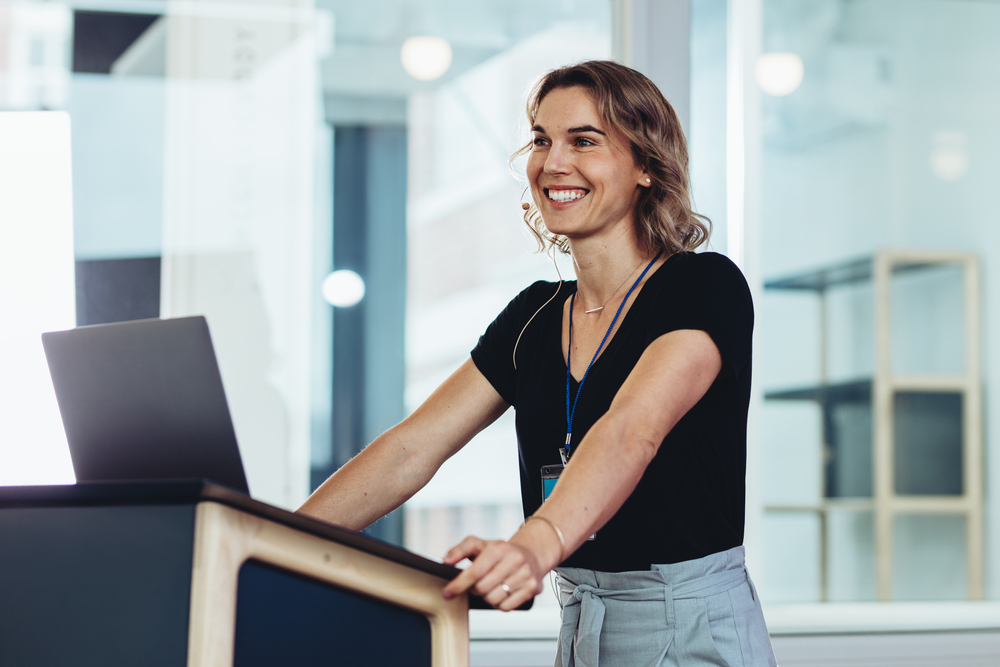 Businesswoman,Standing,At,Podium,With,Laptop,And,Smiling.,Successful,Female